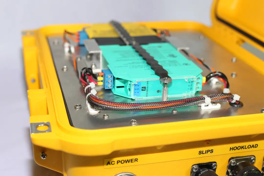 Open Remote Unit showing green intrinsically safe barrier modules and a braided wiring harness on a metal plate, above case connectors labelled AC power, slips and hookload.